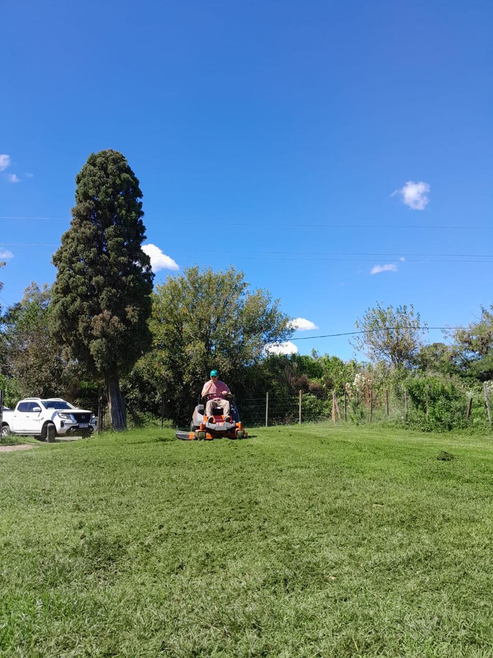 Operario de Oliverde cortando el pasto en una quinta con la camioneta de trabajo al fondo